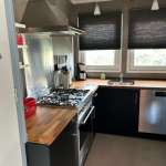 Modern L-shaped kitchen with stainless steel stove, vent hood, and wooden butcher-block counters beneath black cabinets.