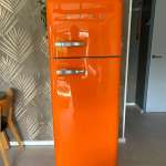 Bright orange retro SMEG fridge with freezer on top in a modern kitchen setting.