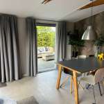 Bright dining area with a dark tabletop and wooden legs, grey chairs, a metallic pendant light, and a glass door leading to the patio outdoor seating area.