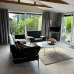 Modern living room with black leather sofas, a round marble coffee table, and a light beige rug in front of large windows with gray curtains.